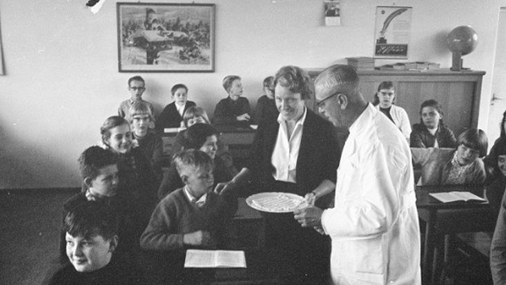 Dr P. Brouwer und seine Assistentin verteilen Zuckerwürfel an Schülerinnen und Schüler
